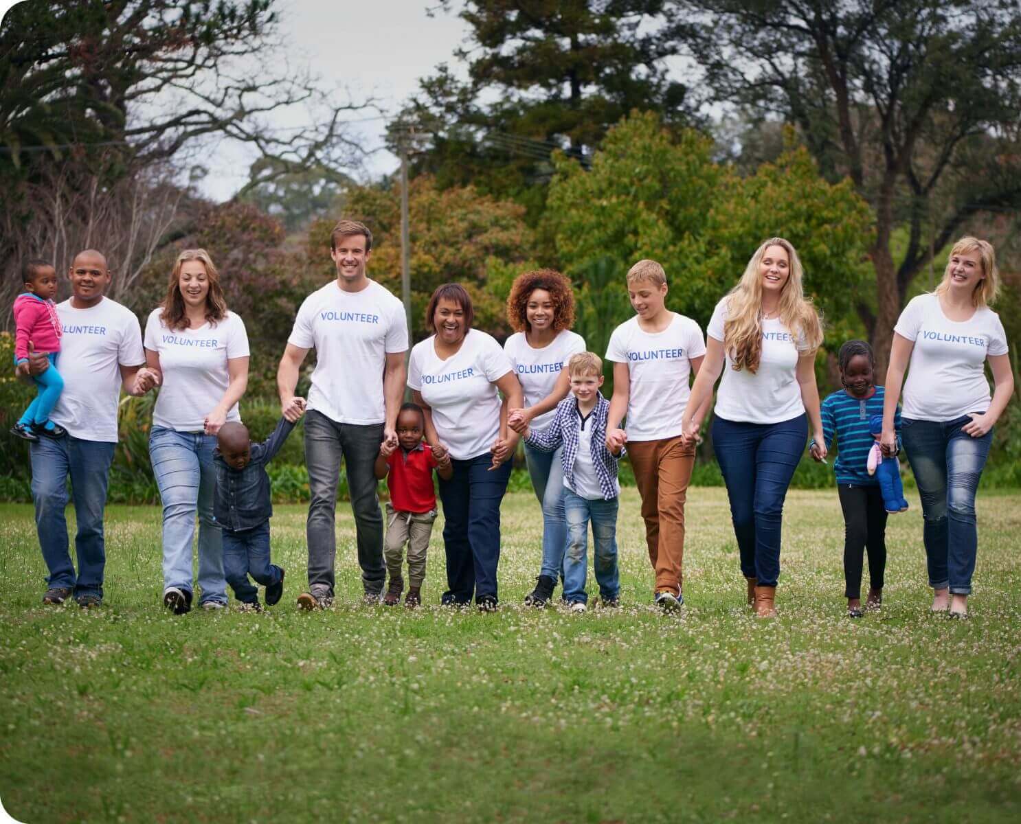 Volunteers holding children's hands walking in park